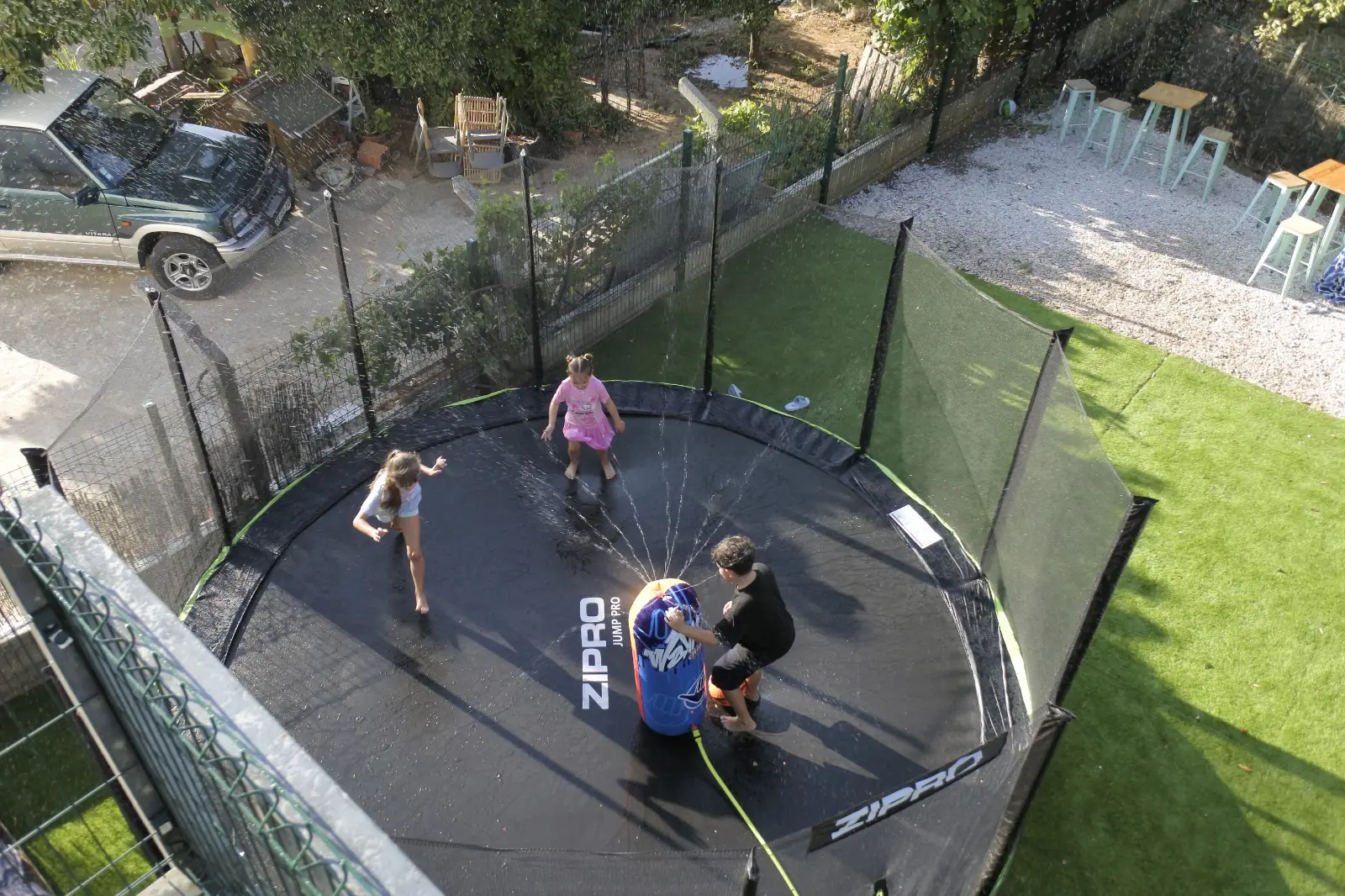 Aerial view of children playing with the water sprinkler on Zazoo's big trampoline
