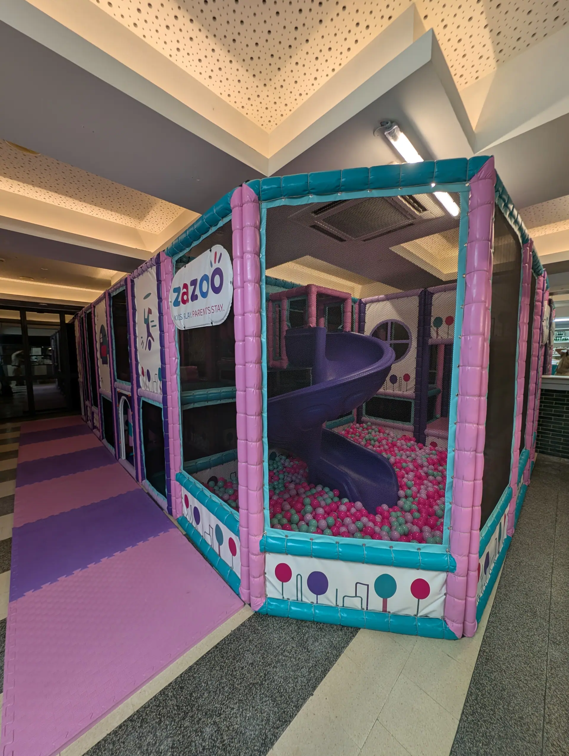 Zazoo's pink, teal and purple indoor soft play frame, with a purple spiral slide dropping into the ball pit